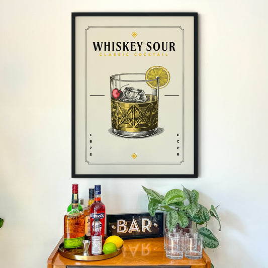 a framed poster of a whiskey sour cocktail hanging on a wall above a wooden bar counter with various liquor bottles and glasses.