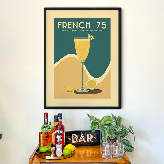 a framed poster of a French 75 cocktail, with a wooden bar cart below it. The poster displays a glass of French 75, a lemon slice, and a bottle of botanical gin champagne lemon juice.