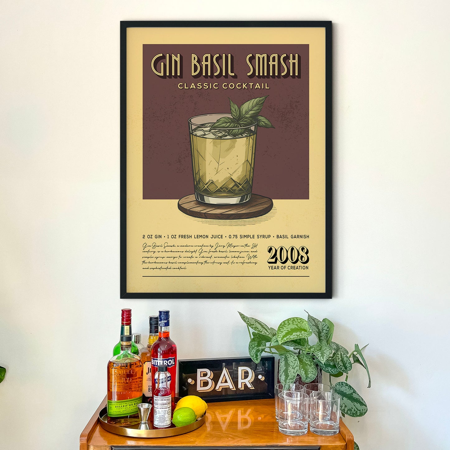 a framed poster of a Gin Basil Smash cocktail hanging on a wall above a wooden bar counter with various liquor bottles and glasses.