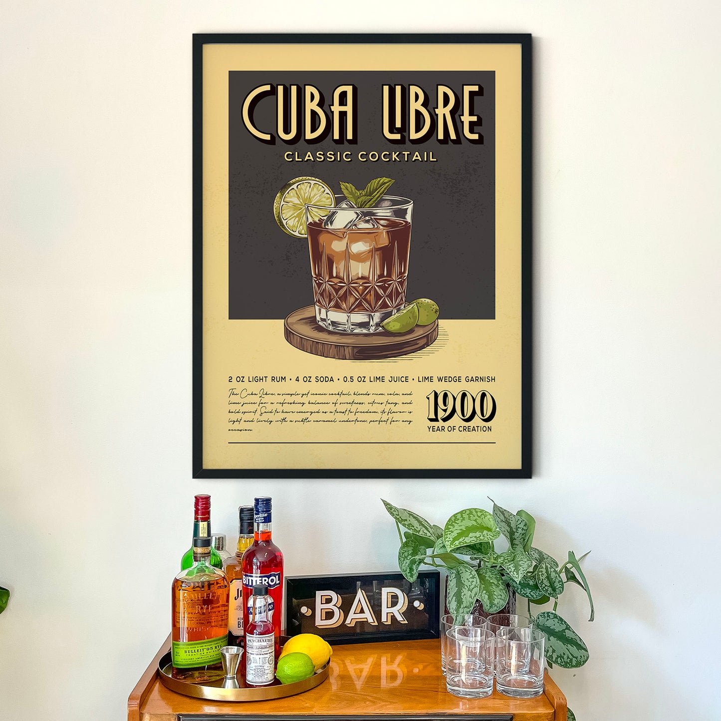 a framed poster of a classic Cuban cocktail recipe, hanging on a wall above a wooden bar counter with various liquor bottles and glasses.