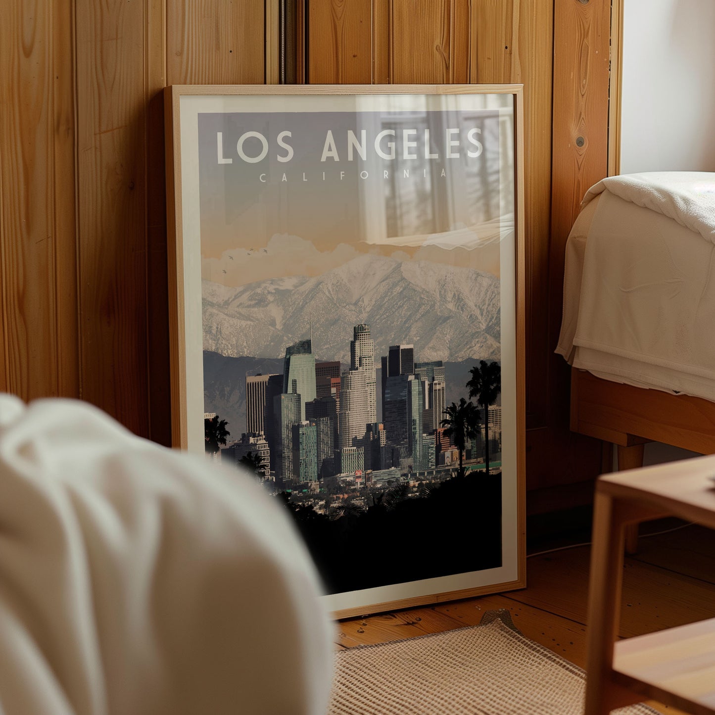 A framed poster of the Los Angeles skyline, with mountains in the background, is displayed in a room with wooden walls.