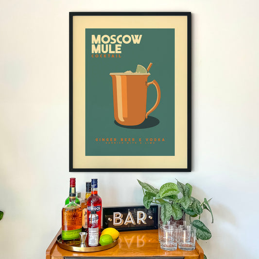 a framed poster of a Moscow Mule cocktail hanging on a wall above a wooden bar counter with various liquor bottles and glasses.