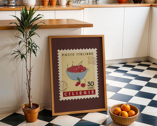 a framed poster of a stamp with a picture of cherries and text, placed on a checkered floor next to a potted plant and a basket of oranges.