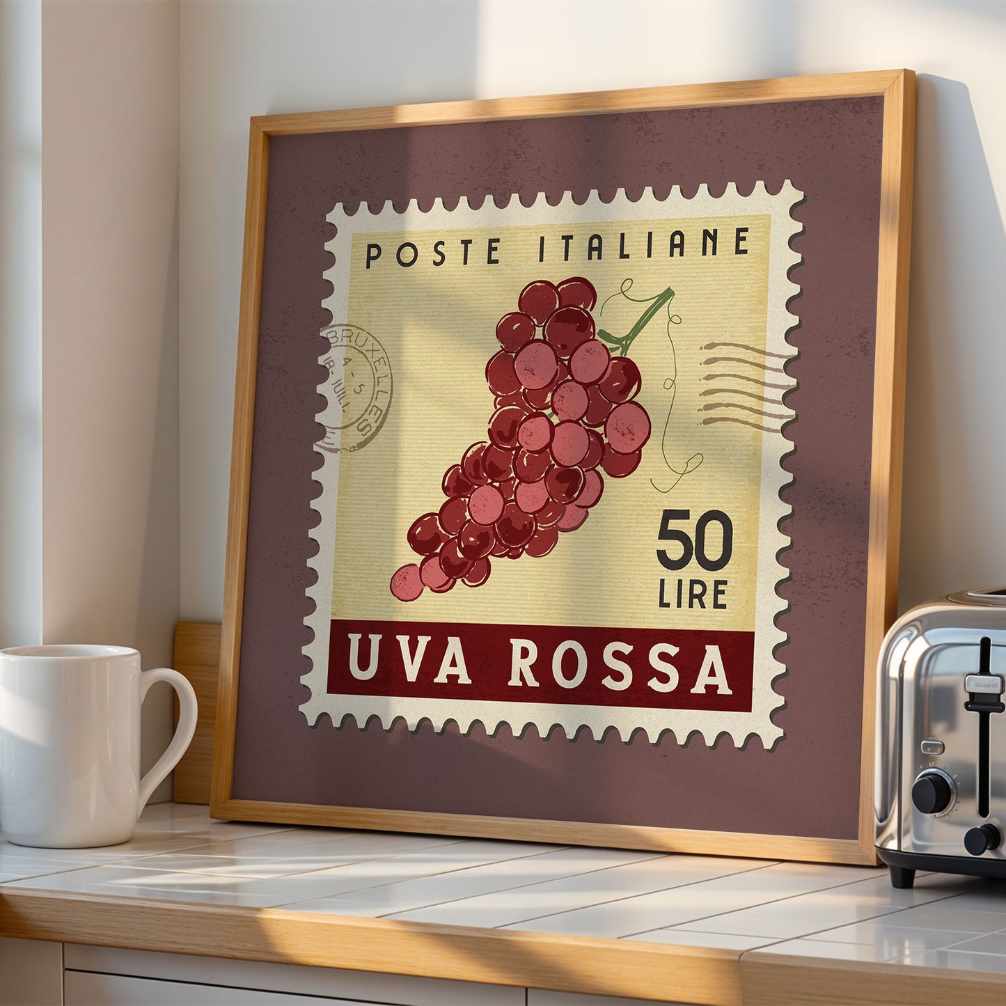 a framed stamp-like artwork depicting a bunch of red grapes, with the text "POSTE ITALIANE 50 LIRE UVA ROSSA" printed on it. The artwork is displayed on a shelf next to a toaster.