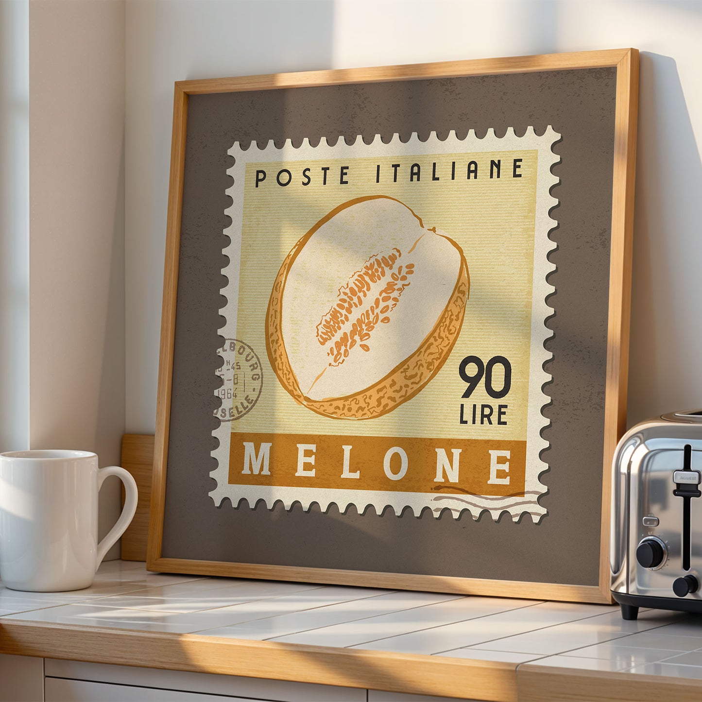 a framed Italian postage stamp with a melon on it, placed on a kitchen counter next to a toaster.