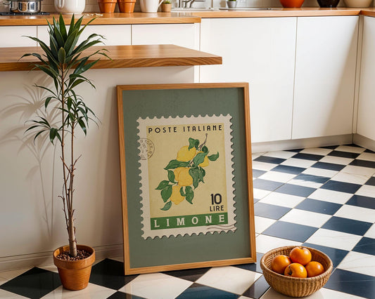 a framed stamp-like artwork depicting a lemon, placed on a checkered floor next to a potted plant and a basket of oranges.