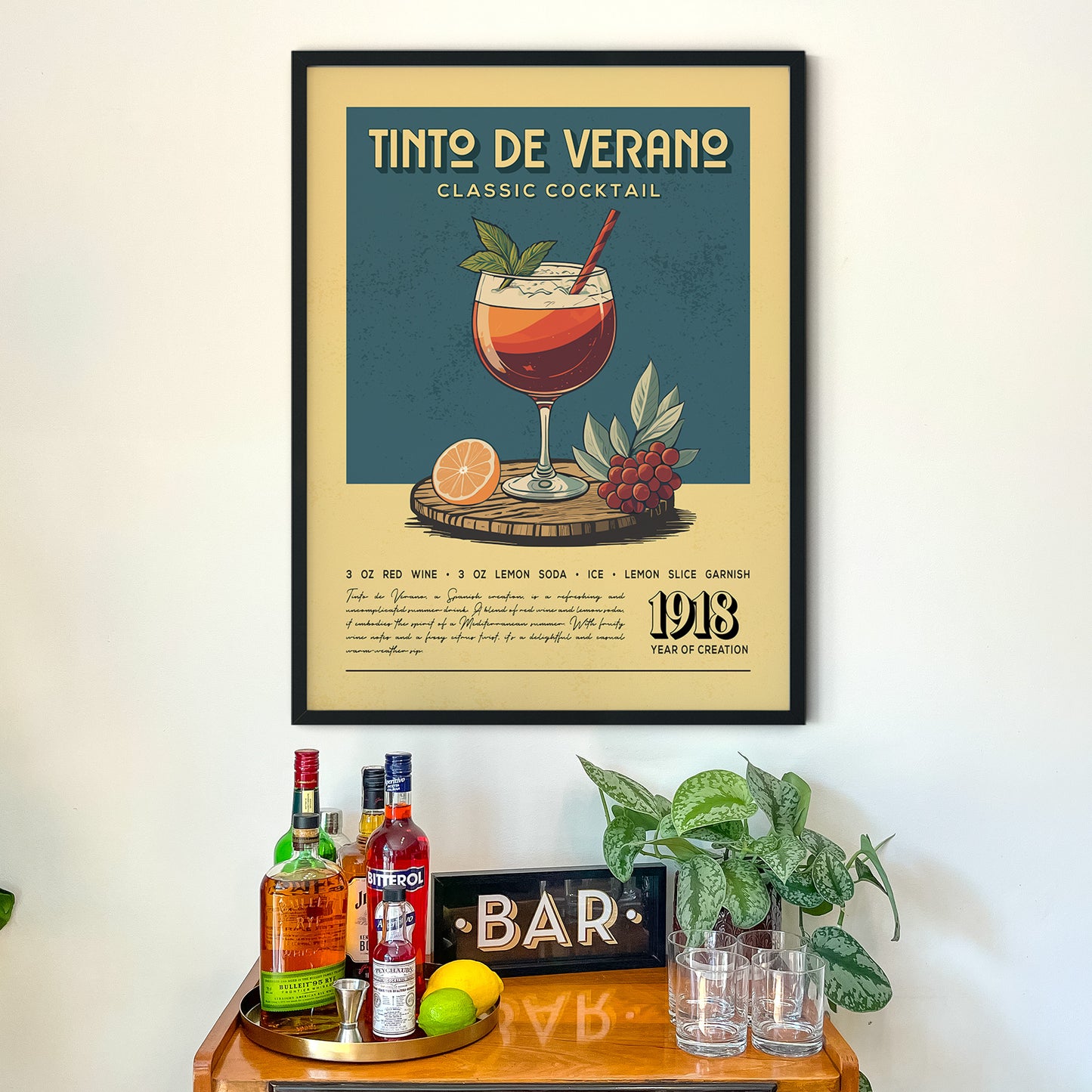 a framed poster of a Tinto de Verano cocktail on a wall above a wooden bar counter with various liquor bottles and glasses.