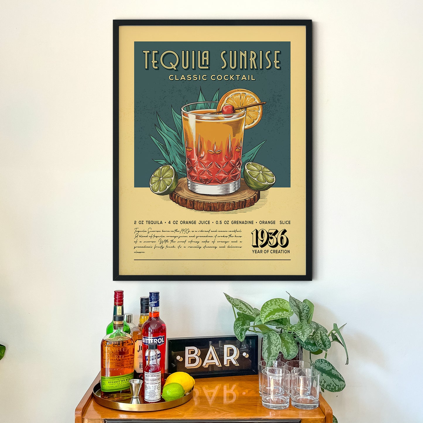a framed poster advertising a "Tequila Sunrise Classic Cocktail" on a wall above a wooden bar counter with various liquor bottles and glasses.