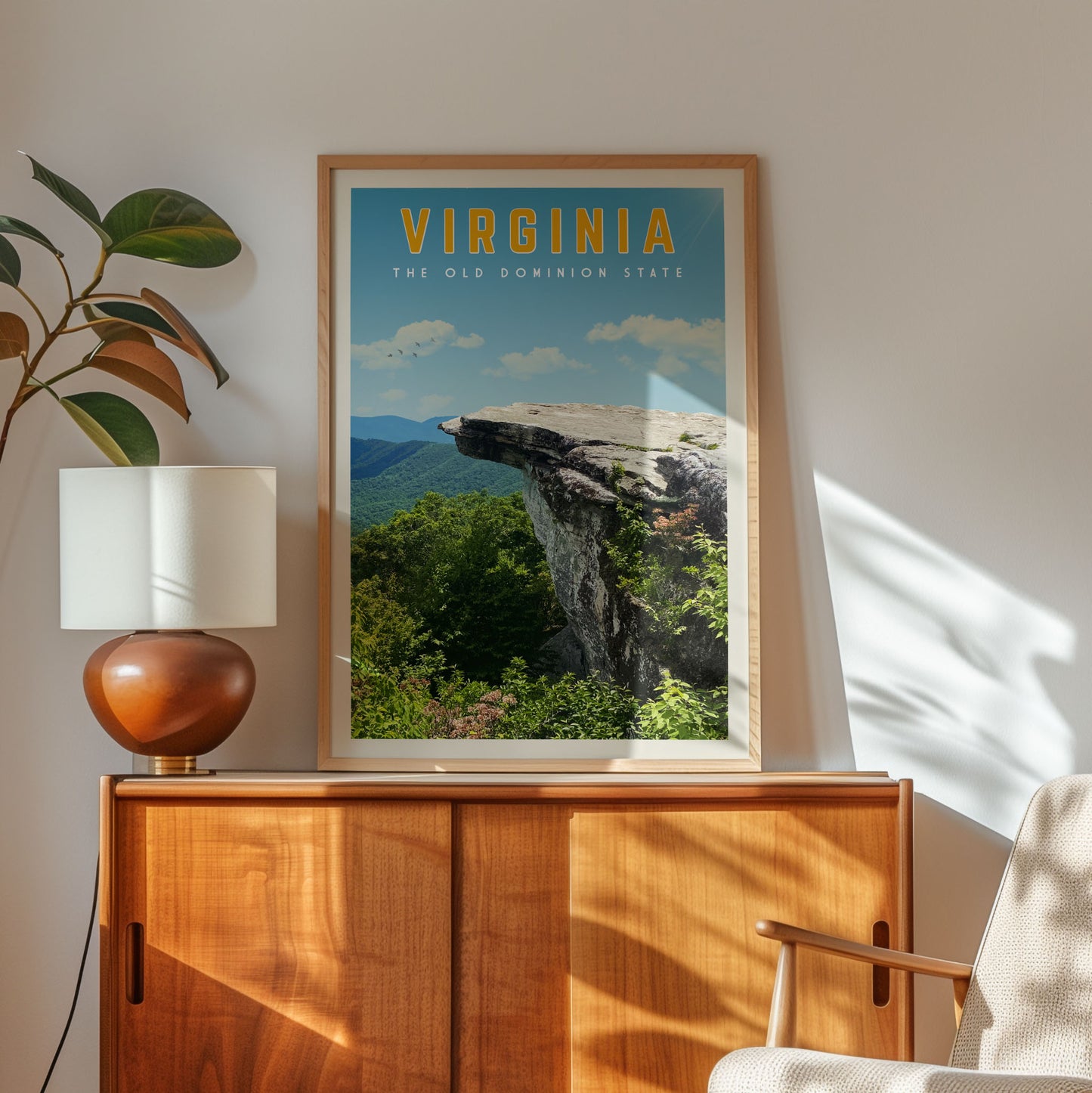 a framed poster of a scenic mountain landscape with the text "VIRGINIA THE OLD DOMINO STATE" on it, placed on a wooden cabinet in a room with a lamp and a plant.