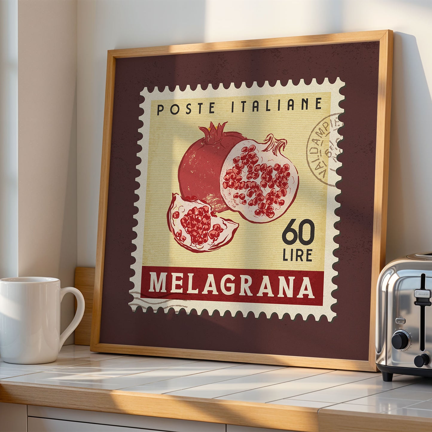 a framed vintage postage stamp with an illustration of pomegranates, placed on a counter next to a toaster.