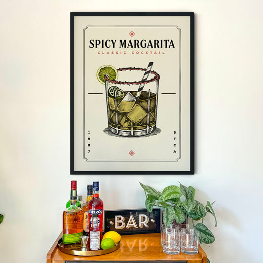 a framed poster of a Spicy Margarita cocktail hanging on a wall above a wooden bar counter with various liquor bottles and glasses.
