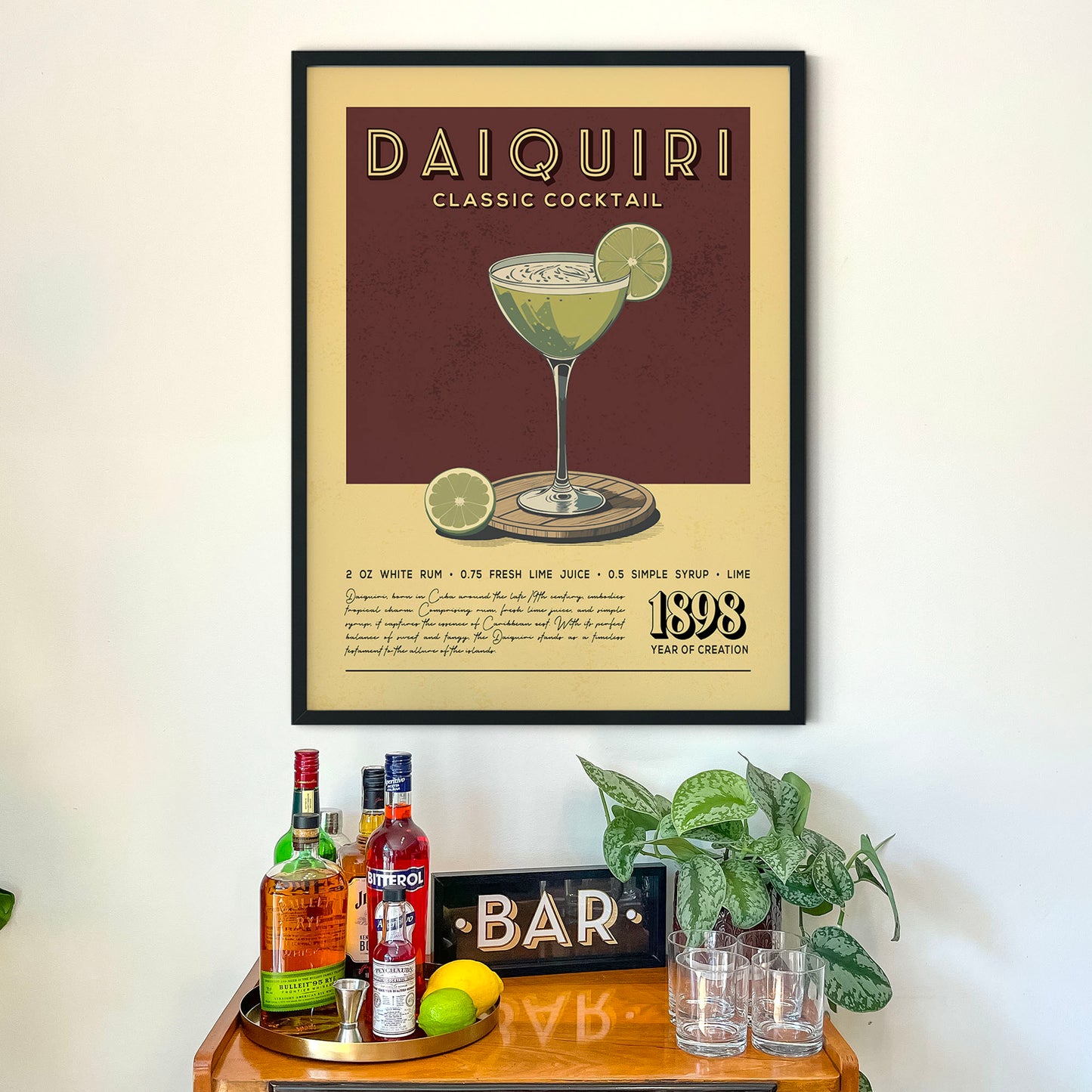 a framed poster of a Daiquiri cocktail on a wall above a wooden bar counter with various liquor bottles and glasses.