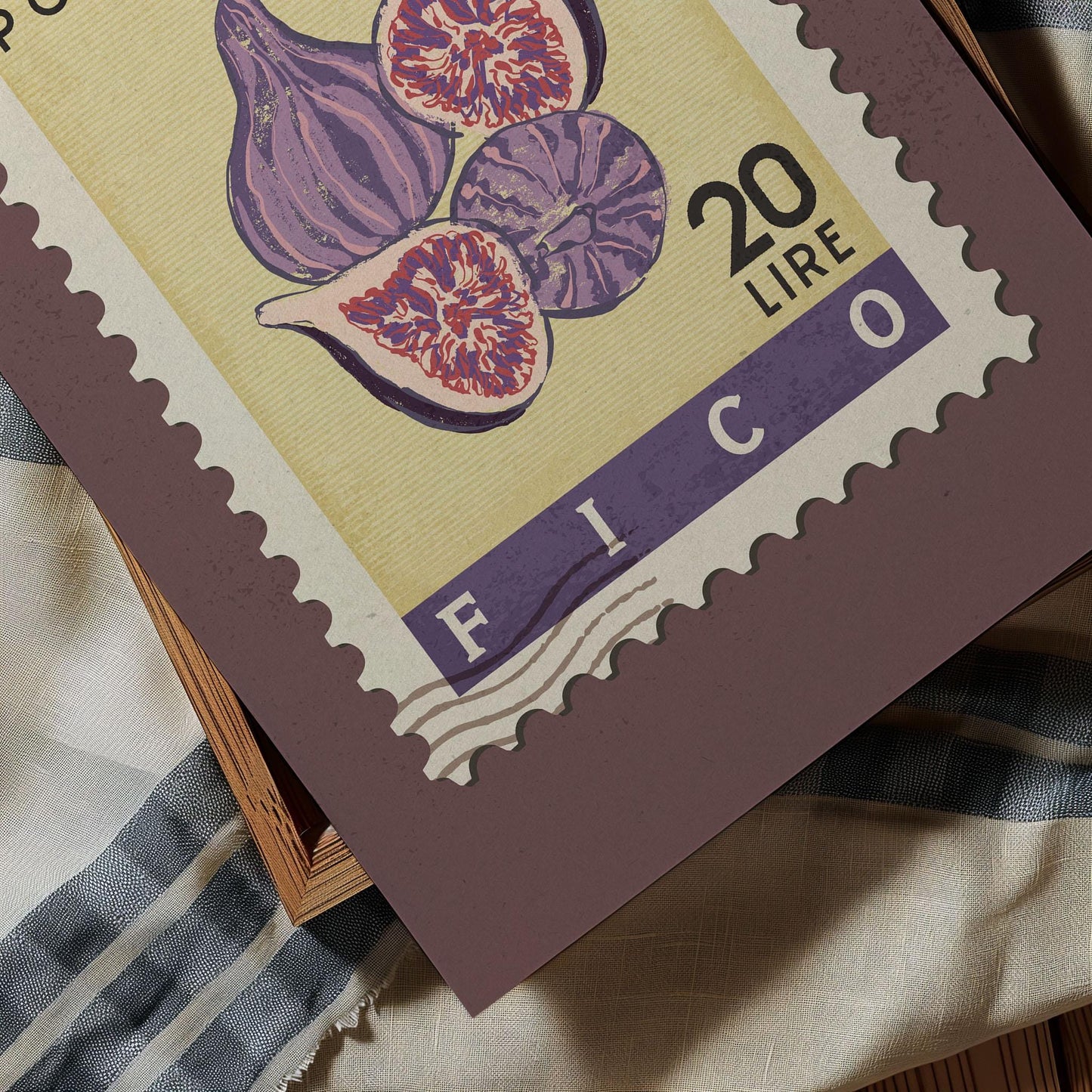 a close-up of a postage stamp with a purple and yellow design, depicting purple figs. The stamp has a value of 20 lire and is placed on a surface with a striped fabric.