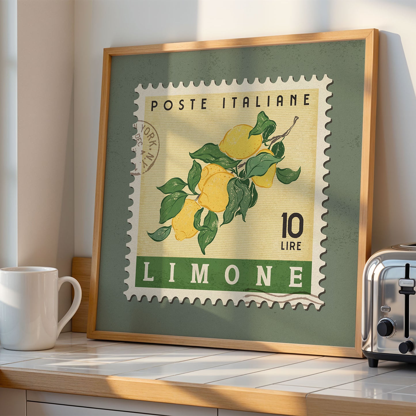 A framed stamp-like artwork depicting a lemon tree on a kitchen counter, with a white mug and a toaster visible in the background.