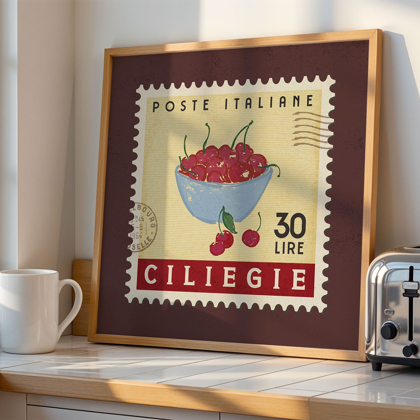 a framed stamp-like artwork depicting a bowl of cherries, with the text "POSTE ITALIANE 30 LIRE CILIEGIE" printed on it. The artwork is displayed on a kitchen counter, with a toaster and a coffee mug visible in the background.