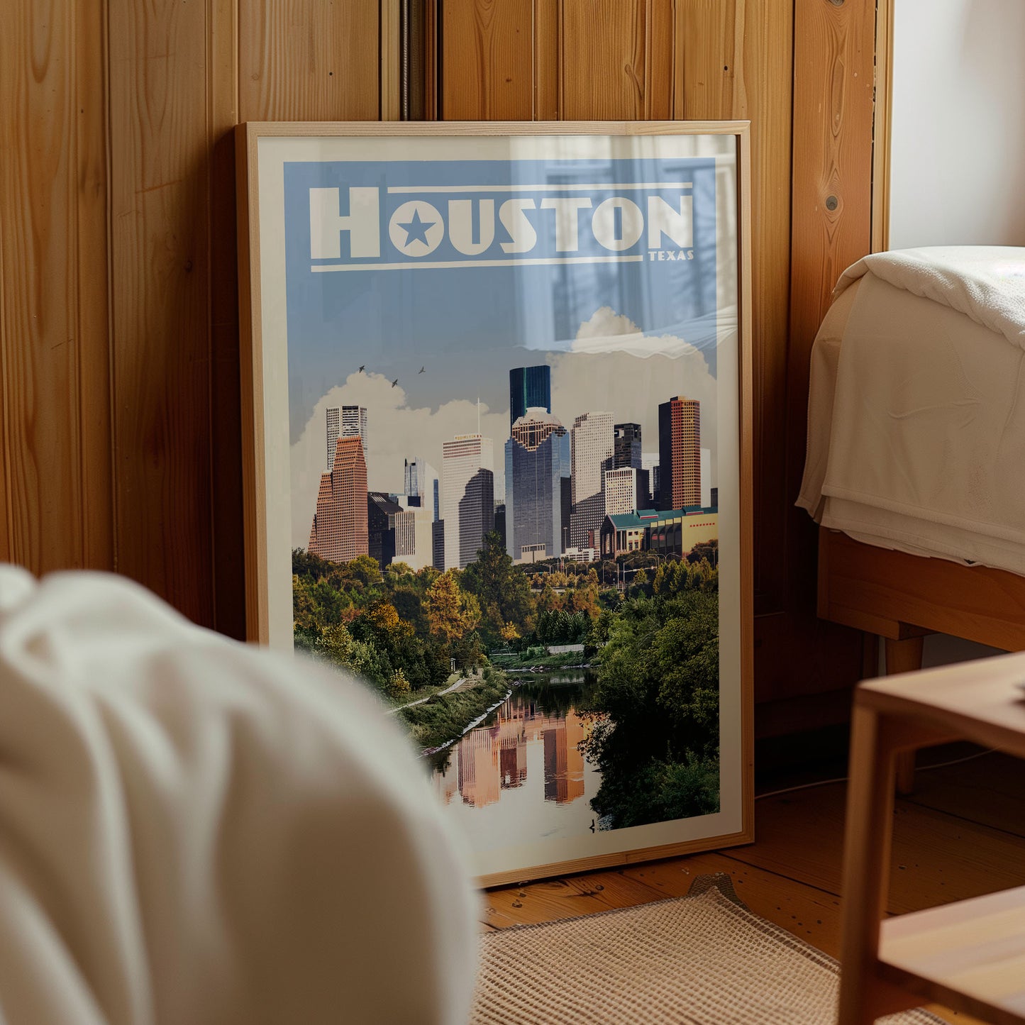 A framed poster of the Houston skyline, with the city's iconic buildings and greenery visible, is displayed in a room with wooden walls.