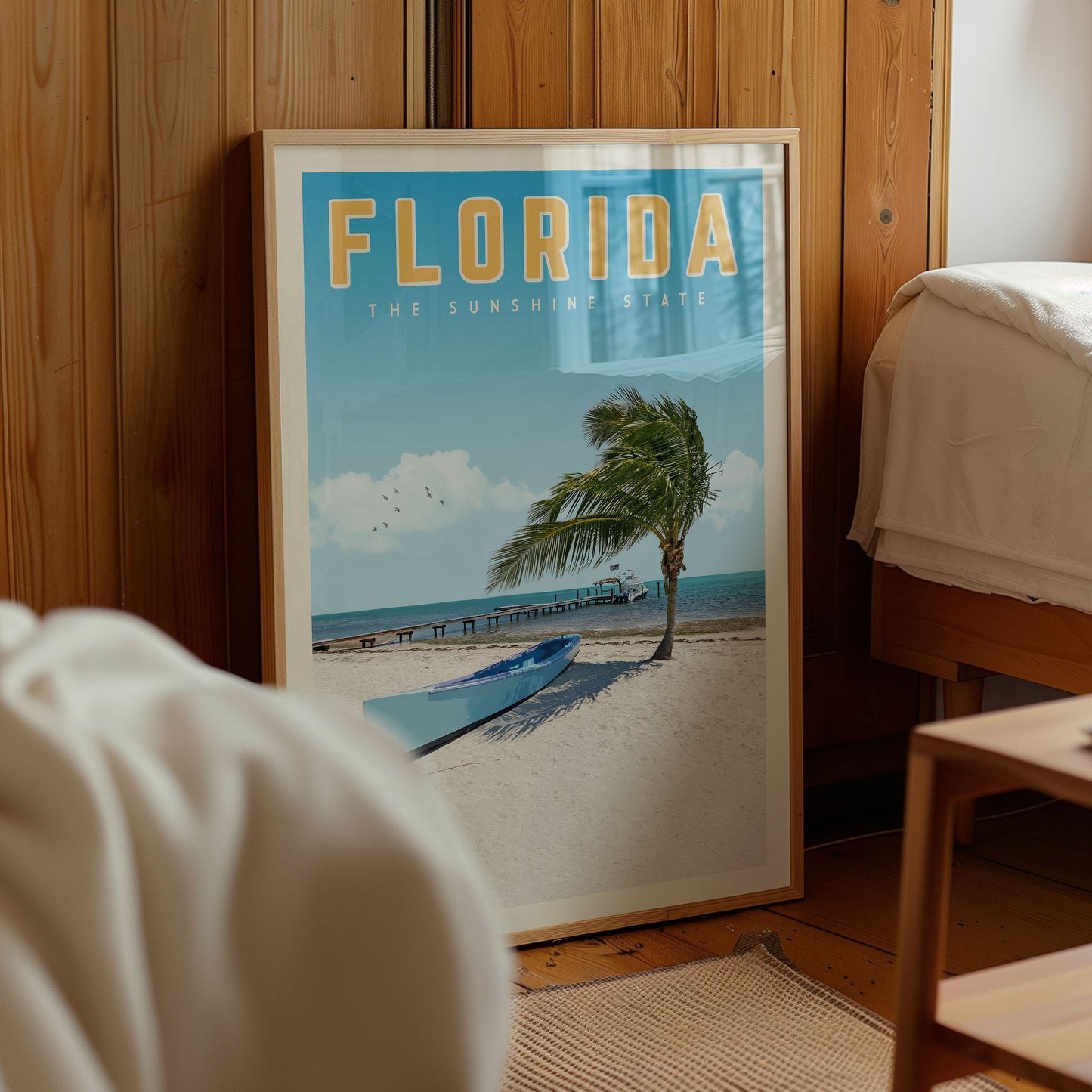 A framed poster of a beach scene with palm trees and a boat on the sand, located in a room with wooden walls.