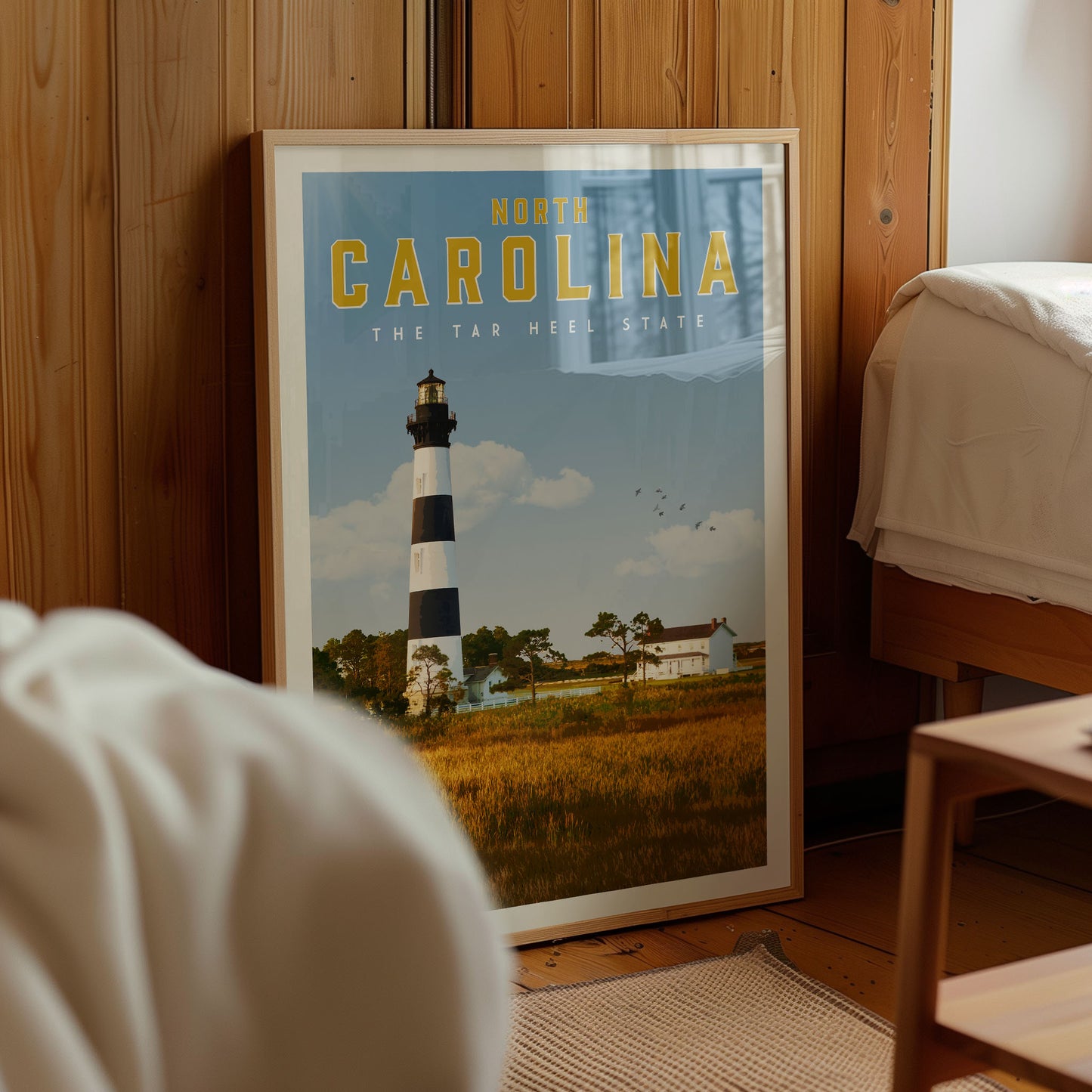 A framed poster of a lighthouse in North Carolina, with a serene landscape of trees and a blue sky in the background.