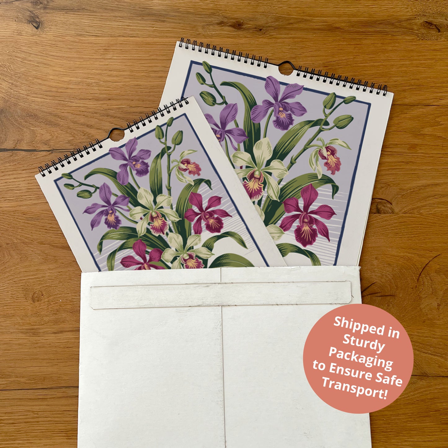 two spiral-bound planners with a floral design, placed inside a white envelope on a wooden surface.