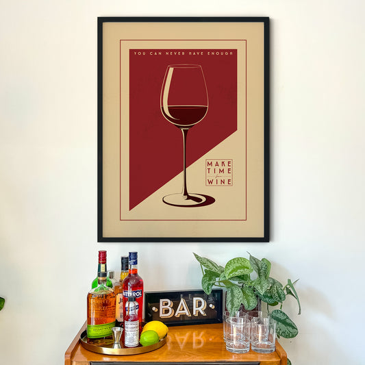 a framed poster with a wine glass illustration, accompanied by the text "You can never have enough wine" and "Make time for wine" on a wooden table below it.