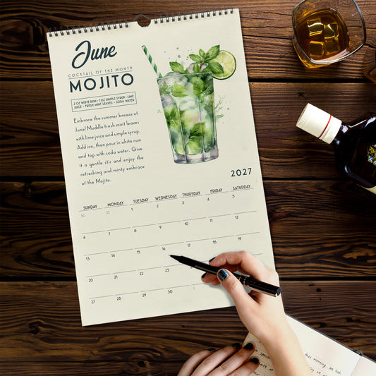 A person is writing in a notebook while holding a pen, with a calendar for the month of June visible on a wooden surface.