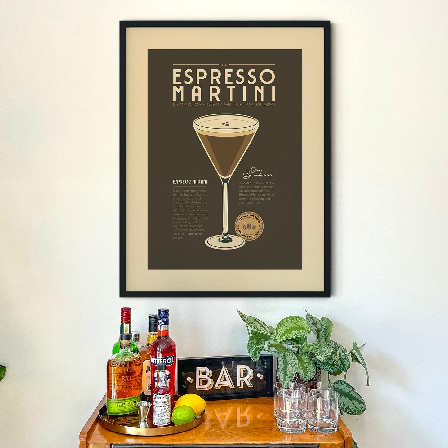 a framed poster of an espresso martini hanging on a wall above a wooden bar cart. The poster includes an illustration of the espresso martini and provides a recipe for making the drink.