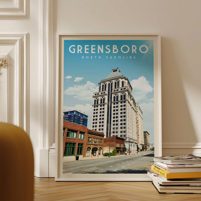 A framed poster of Greensboro, North Carolina, featuring a tall white building with a blue roof against a blue sky with clouds.