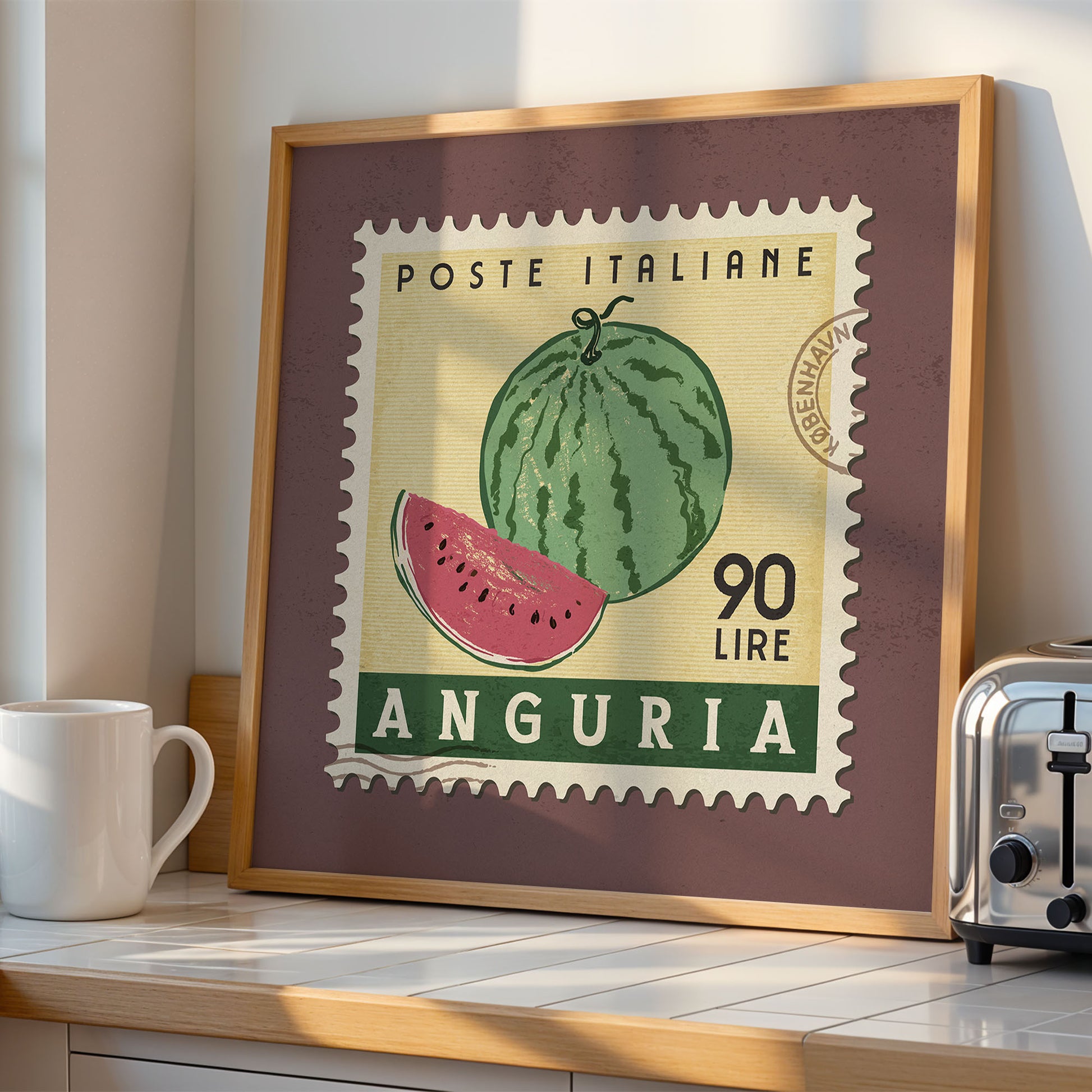 a framed stamp-like artwork depicting a watermelon, with the text "POSTE ITALIANE 90 LIRE ANGURIA" printed on it. The artwork is displayed on a shelf next to a toaster, creating a kitchen-themed setting.