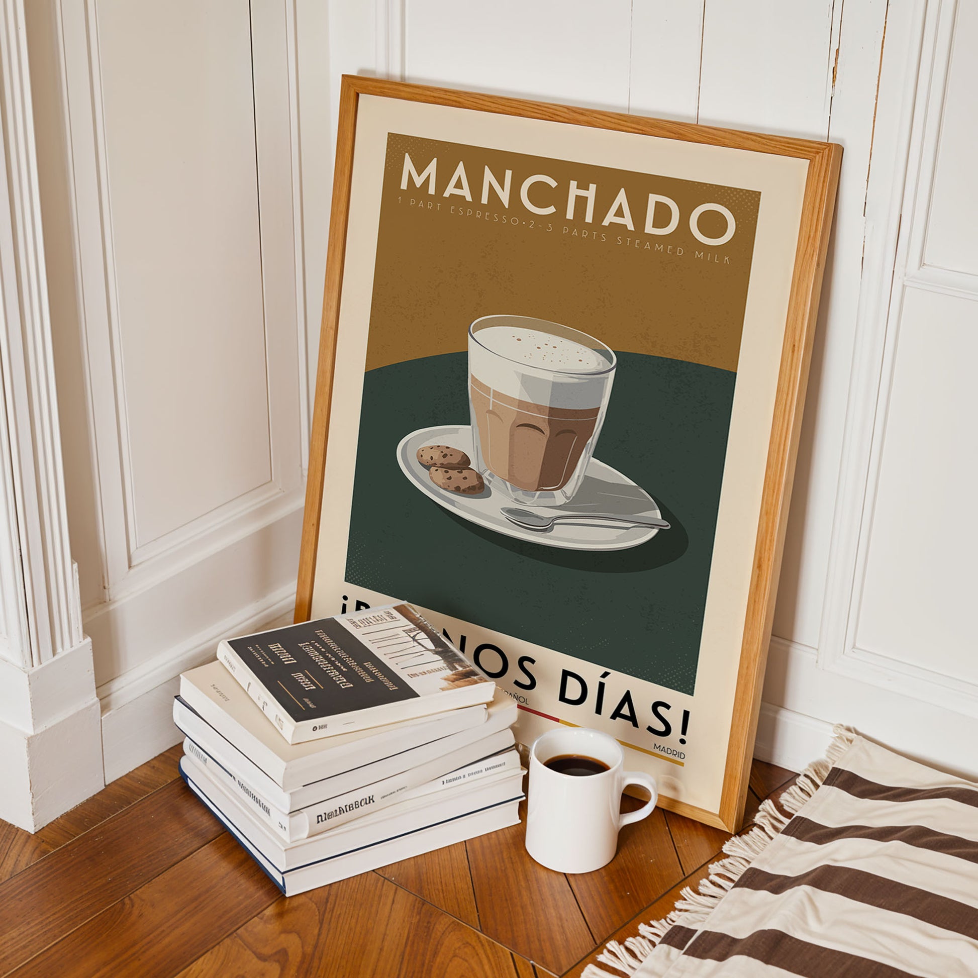 a framed poster of a cup of coffee with cookies, placed on a wooden floor next to a stack of books and a white mug.