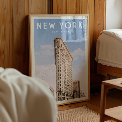 A framed poster of the Flatiron Building, a famous New York skyscraper, is displayed in a room with a wooden wall and a bed visible in the background.