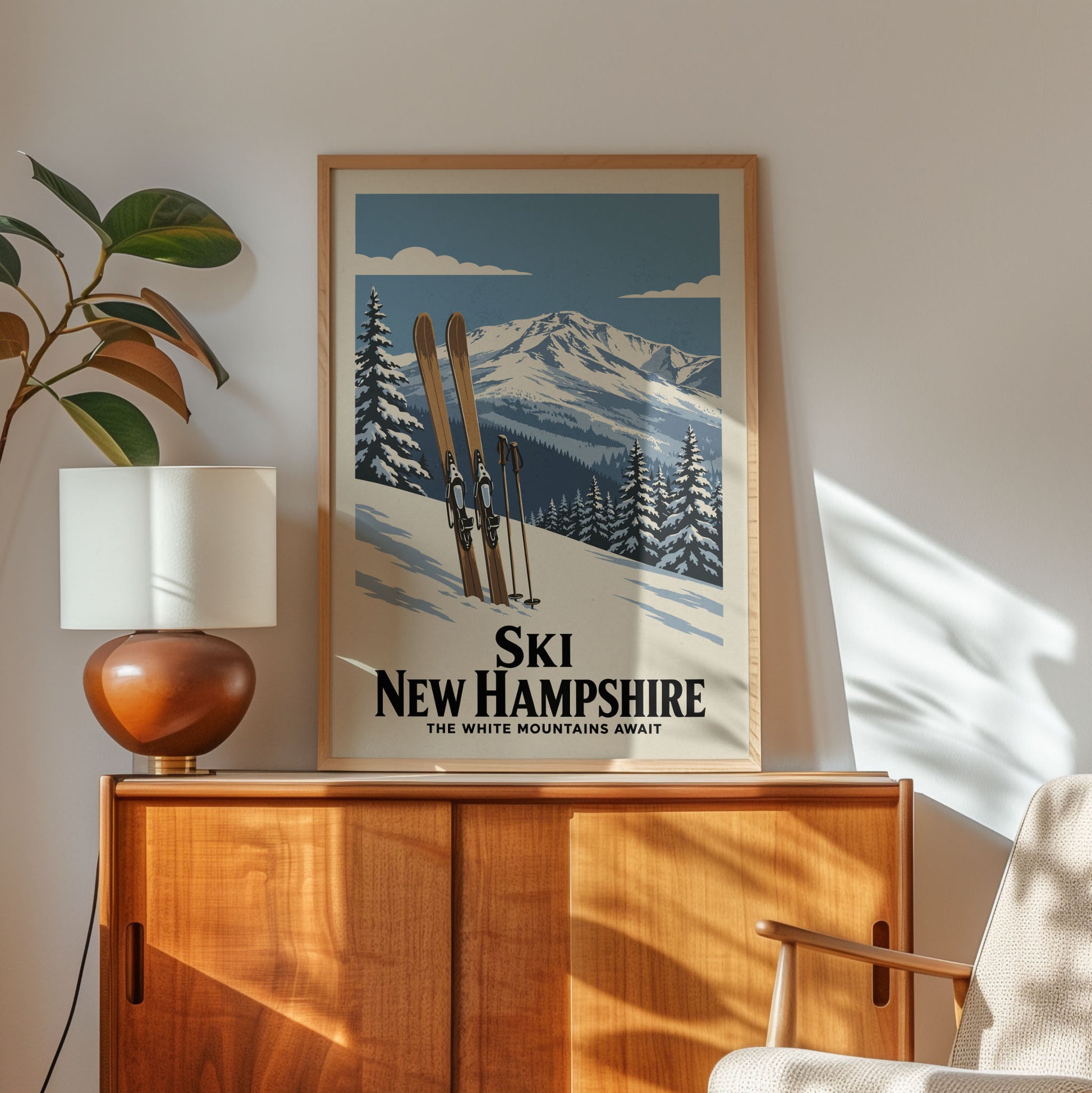 A framed poster of a snowy mountain landscape with skis and trees, hanging on a wall above a wooden cabinet.