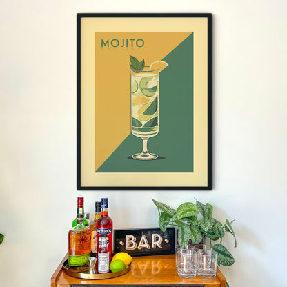 a framed poster of a mojito cocktail hanging on a wall above a wooden bar cart. The poster displays a tall glass filled with a mojito drink, surrounded by various bottles of alcohol and a potted plant.