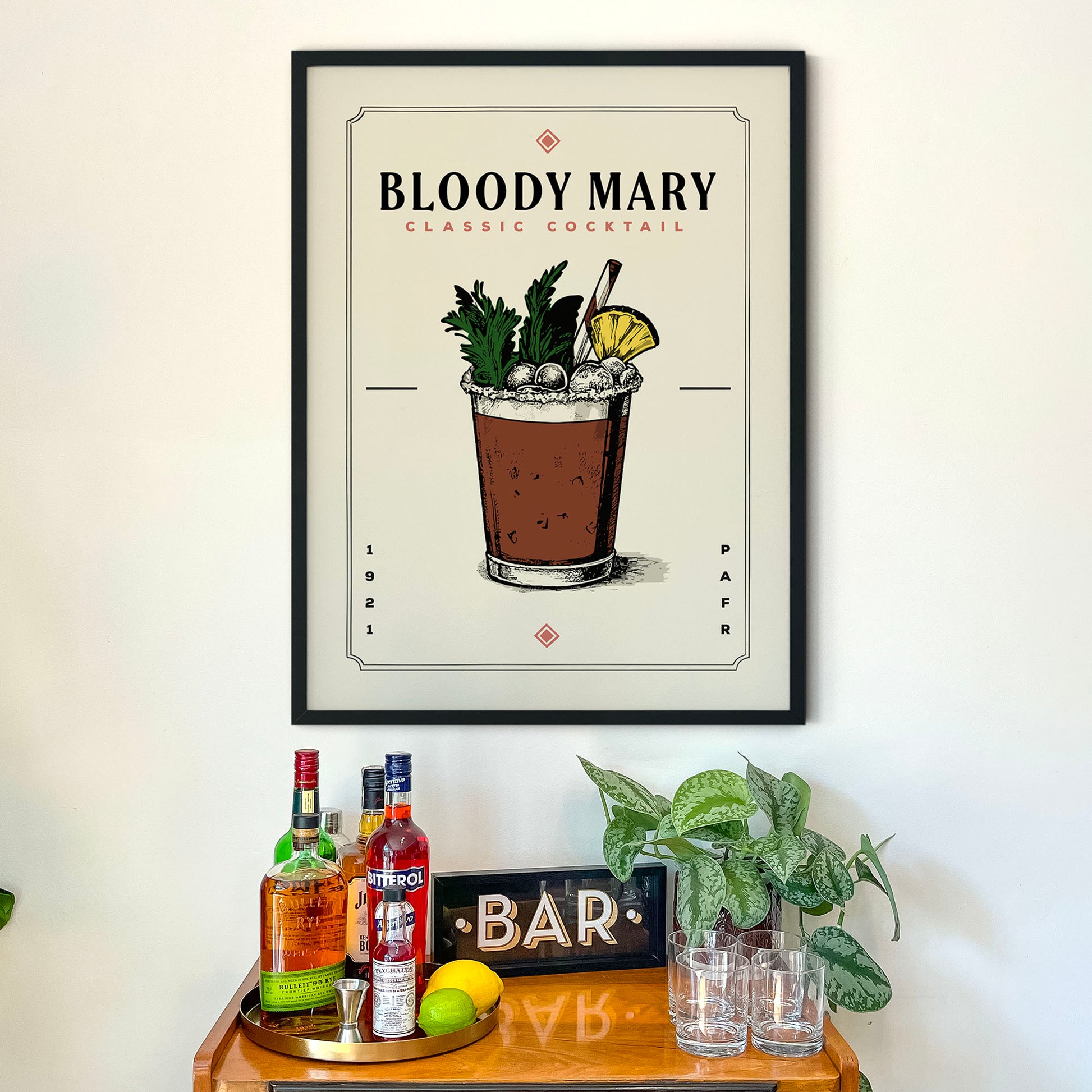 a framed poster of a Bloody Mary cocktail hanging on a wall above a bar cart.