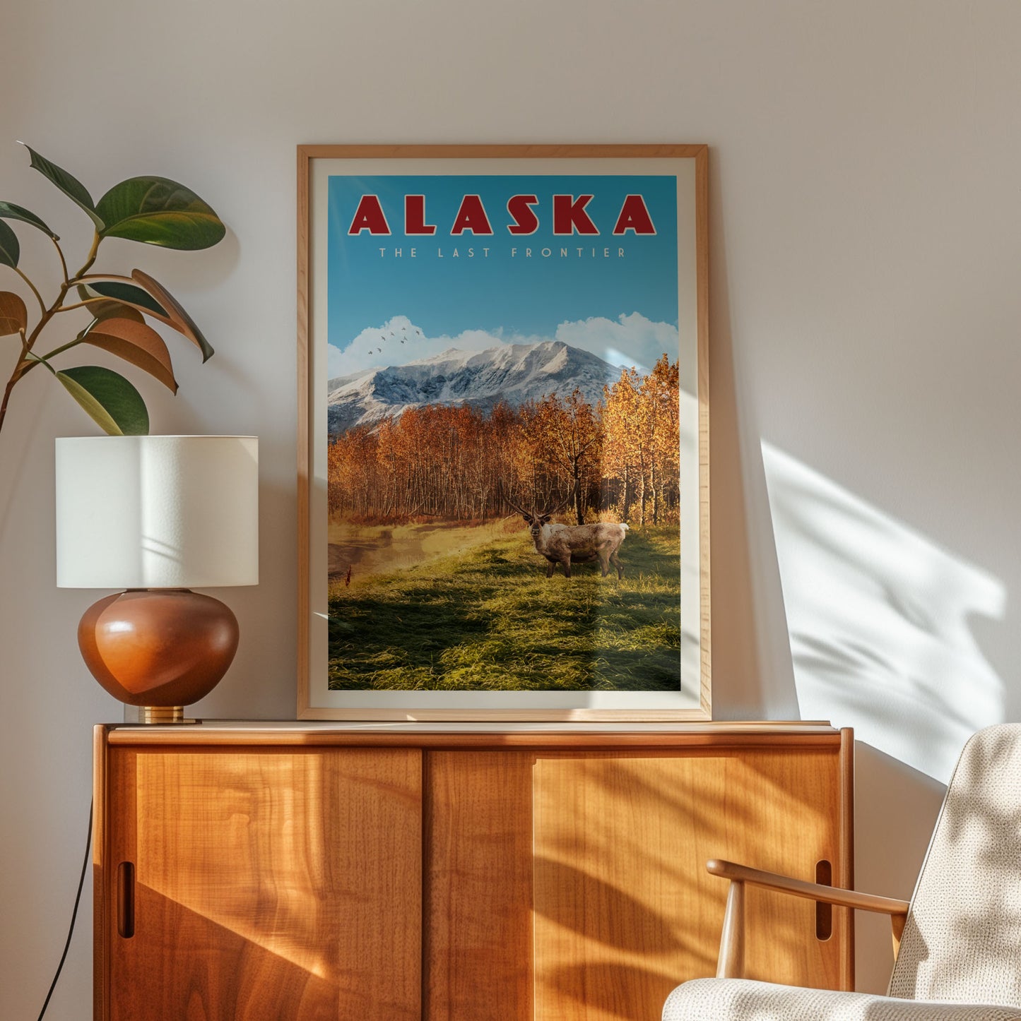 a framed poster of a scenic landscape with mountains and trees, hanging on a wall next to a wooden cabinet and a lamp.