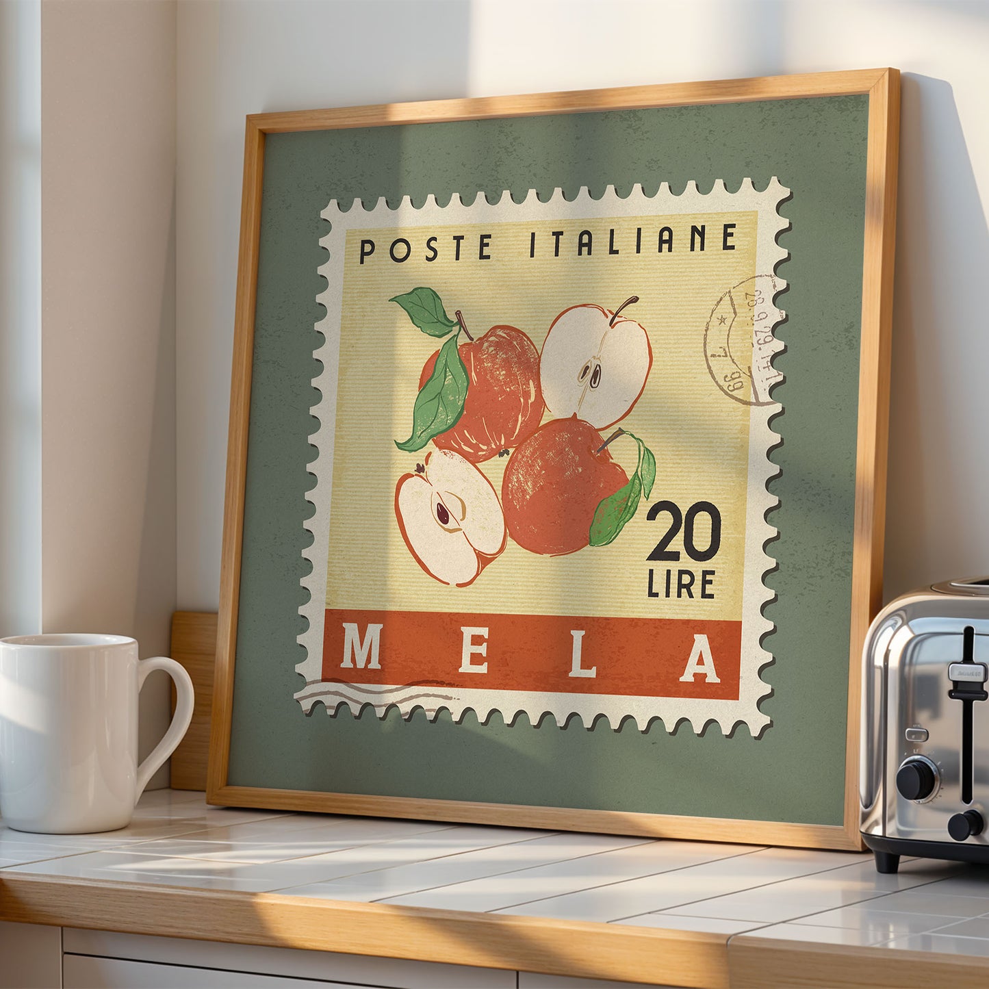 a framed stamp-like artwork depicting a scene with apples, placed on a kitchen counter next to a toaster.