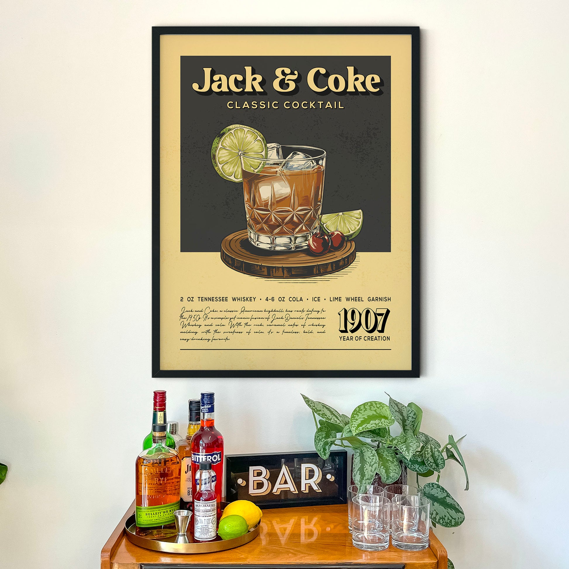 a framed poster of a classic cocktail, specifically the Jack and Coke, hanging on a wall above a wooden bar counter with various liquor bottles and glasses.