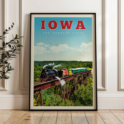 A framed poster of a steam train crossing a bridge over a forest, with the text "IOWA THE HAWKEYE STATE" prominently displayed.