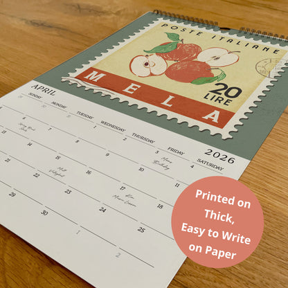 A calendar with a vintage-style stamp design on the cover, featuring an illustration of apples, is placed on a wooden surface.