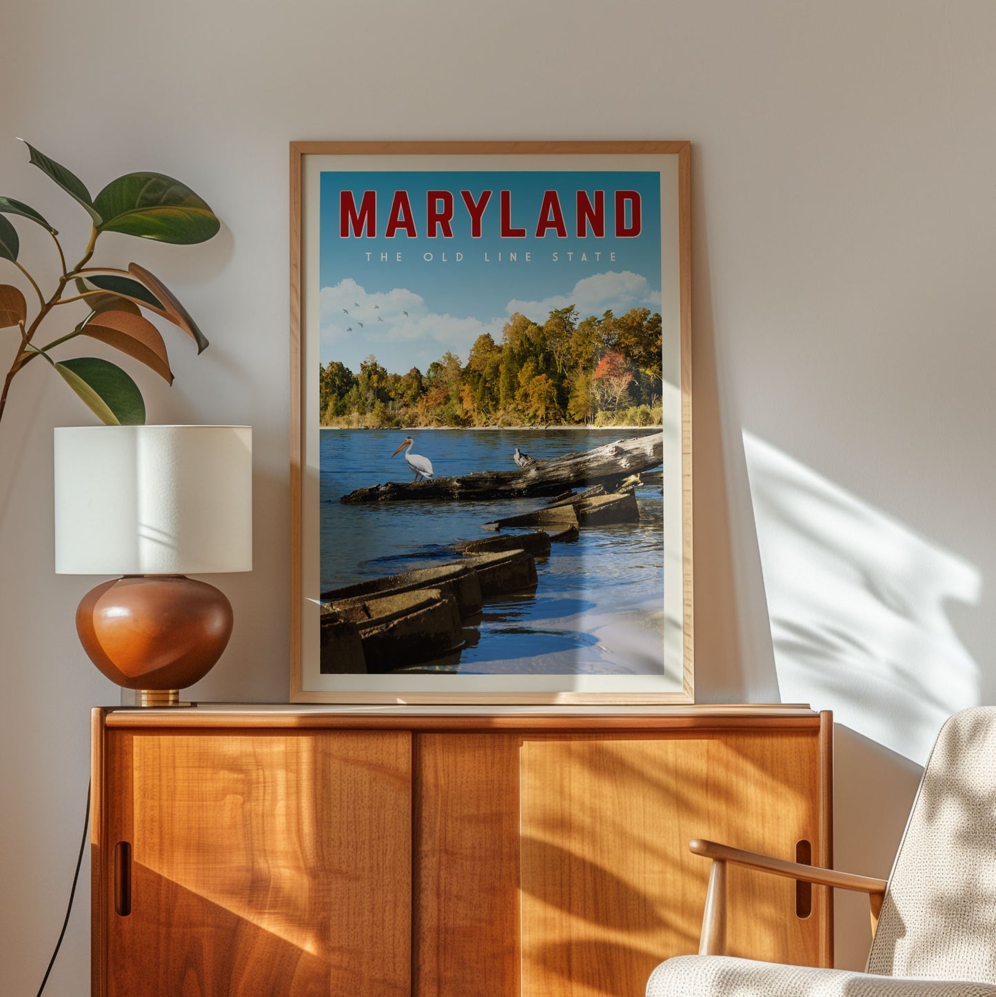 A framed poster of a scenic view of the Chesapeake Bay in Maryland hangs on a wall, with a lamp and a plant to the left of the frame.