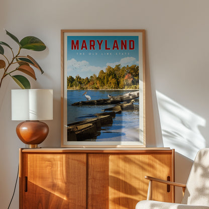 A framed poster of a scenic view of the Chesapeake Bay in Maryland hangs on a wall, with a lamp and a plant to the left of the frame.