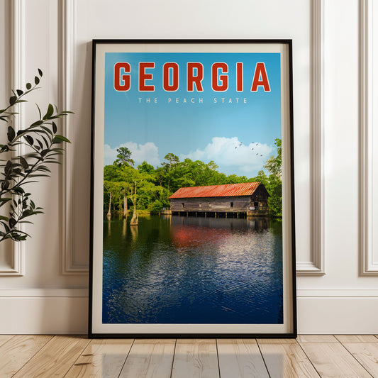 A framed poster of a wooden cabin on a lake, surrounded by trees and a blue sky, with the text "GEORGIA THE PEACH STATE" displayed prominently.
