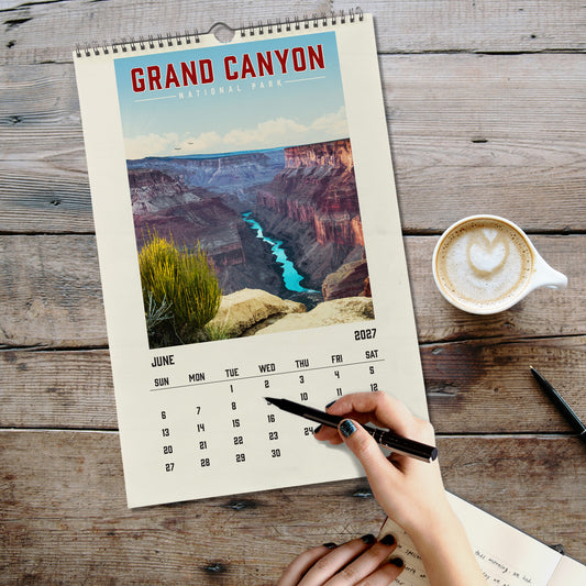 A person's hand is writing in a notebook on a wooden surface, with a calendar for Grand Canyon National Park displayed nearby.