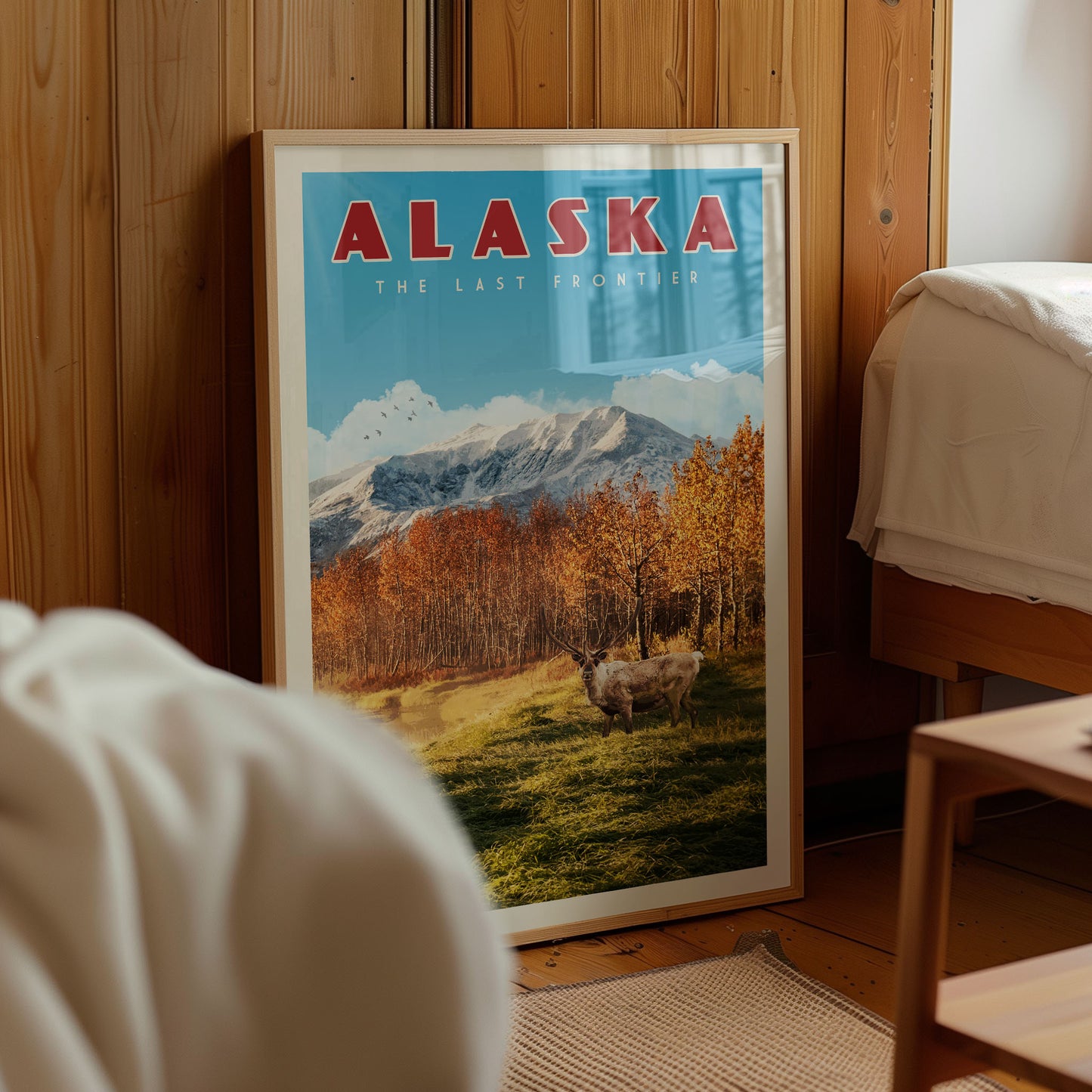 A framed poster of a scenic landscape with mountains, trees, and a herd of animals, including cows, is displayed in a room with wooden walls.