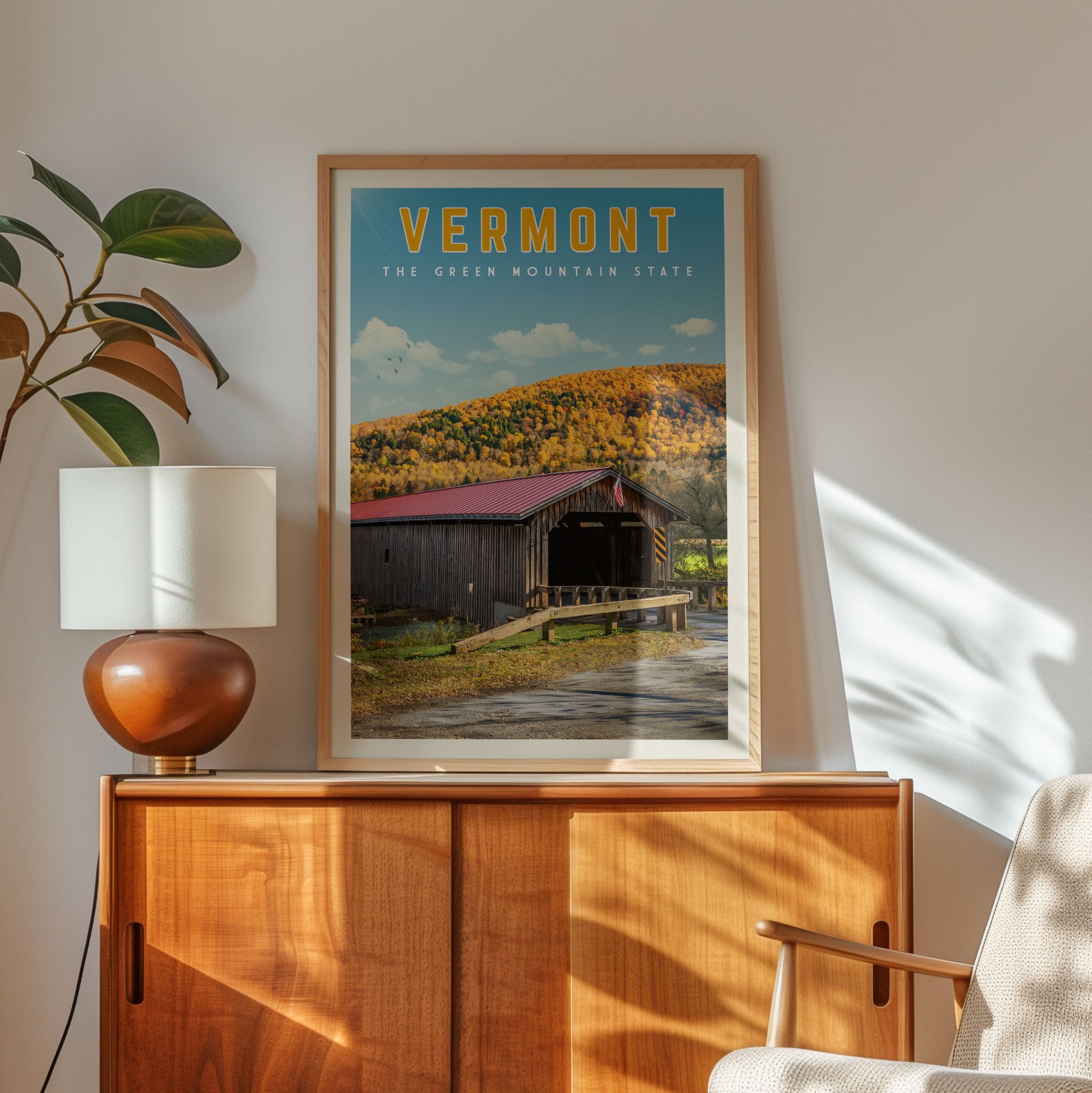 a framed poster of a wooden cabin with a red roof, set against a backdrop of a mountain and trees, hanging on a wall.