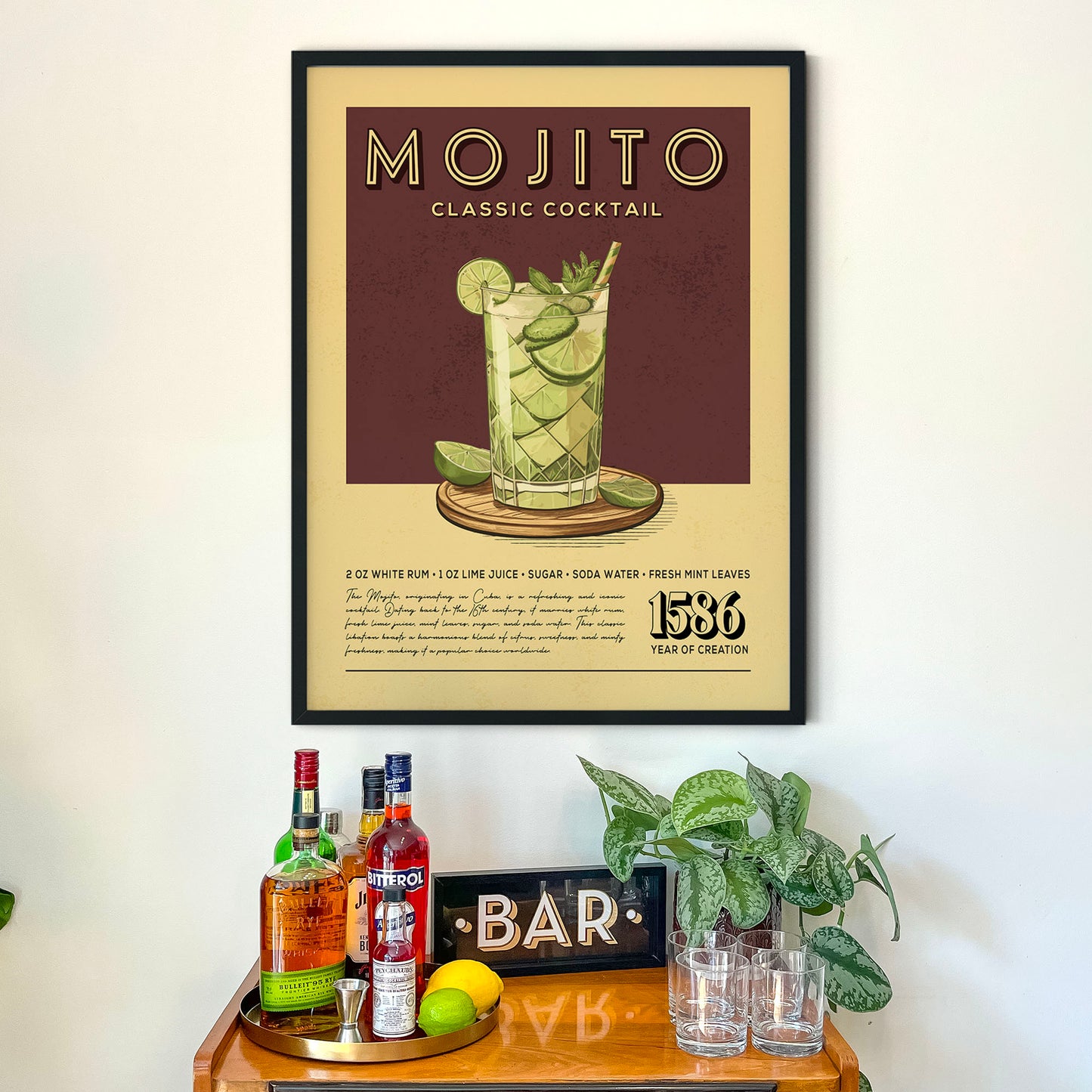 a framed poster of a classic Mojito cocktail hanging on a wall above a wooden bar counter with various liquor bottles and glasses.