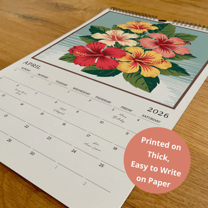 A wall calendar with a floral design on the cover, featuring a variety of colorful flowers. The calendar is printed on paper and is placed on a wooden surface.