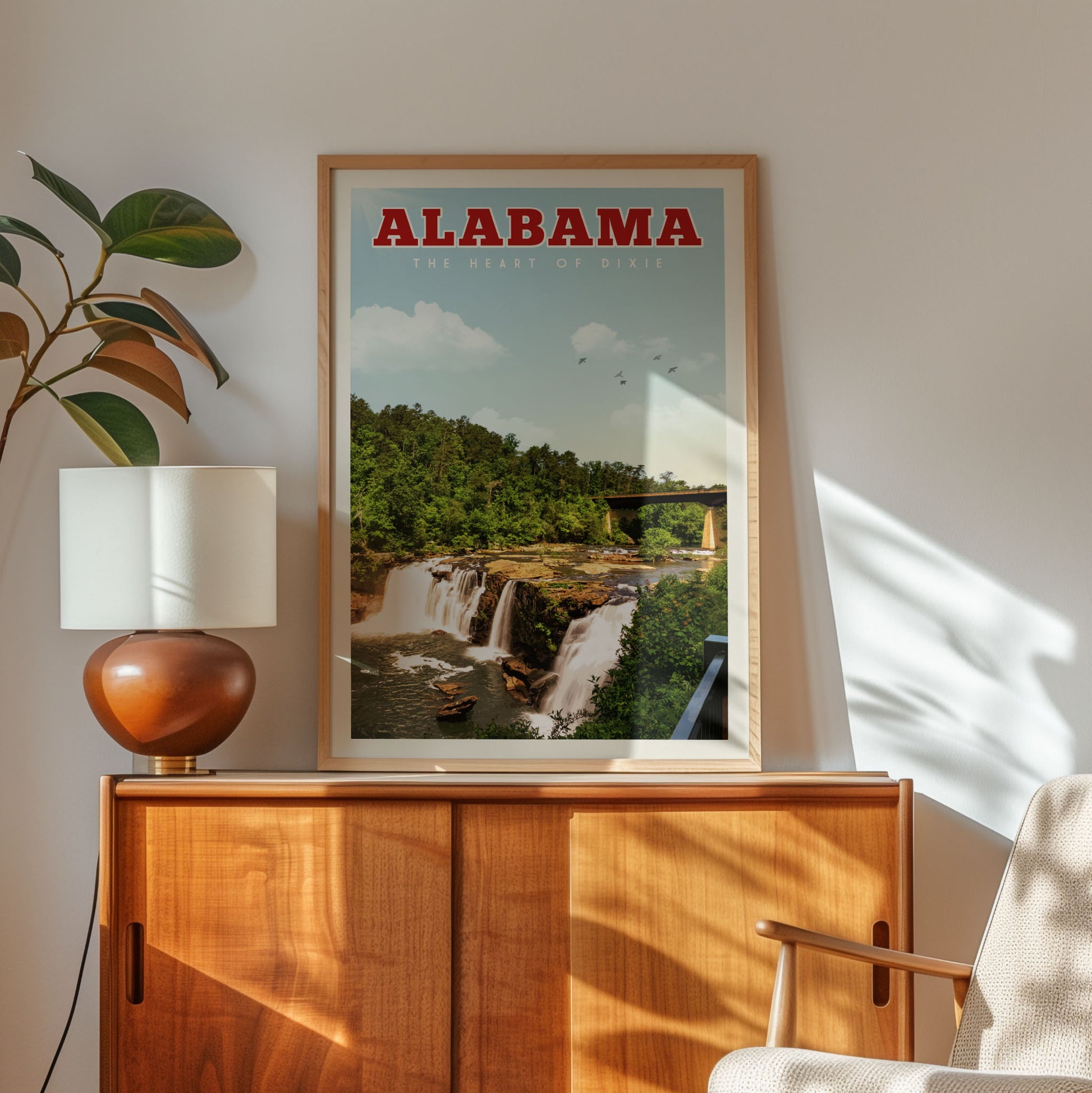 a framed poster of a waterfall in Alabama, with a wooden cabinet and a lamp in the foreground.
