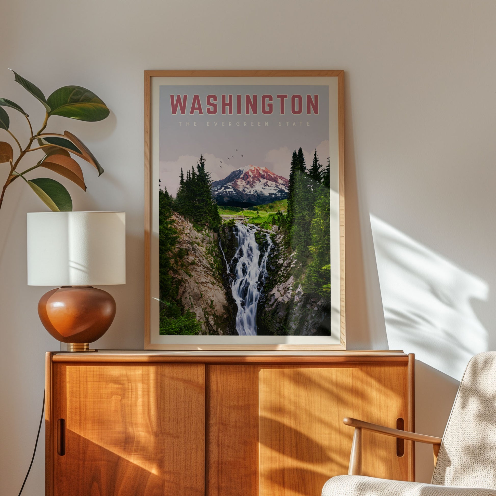 a framed poster of a waterfall and mountain landscape, hanging on a wall next to a wooden cabinet and a lamp.