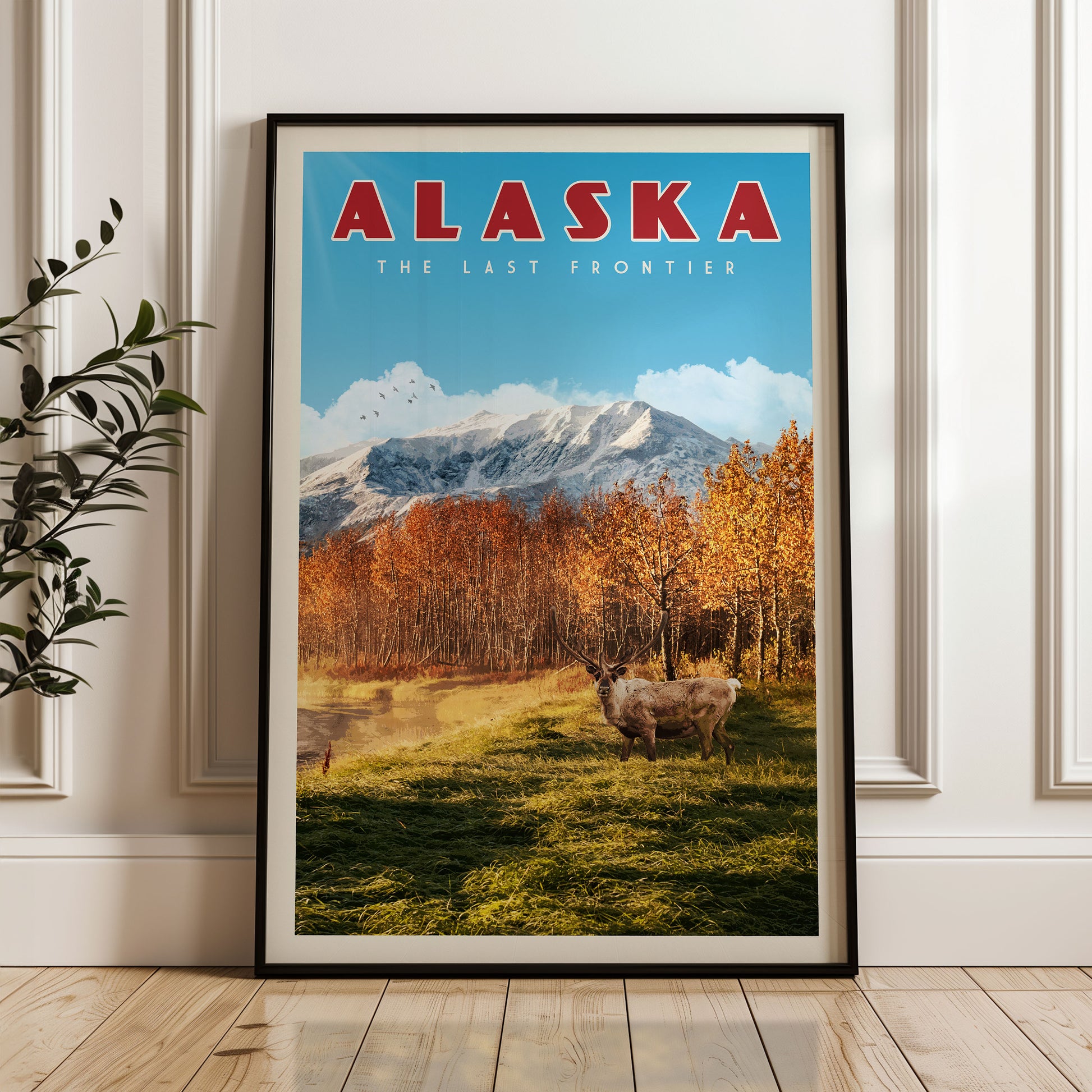 A framed poster of Alaska, featuring a scenic landscape with mountains, trees, and a herd of deer in the foreground.