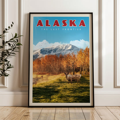 A framed poster of Alaska, featuring a scenic landscape with mountains, trees, and a herd of deer in the foreground.